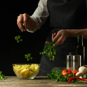 The chef sprinkles with greens, parsley, french fries, on the background with vegetables. Cooking tasty but harmful food. Background for design and menu